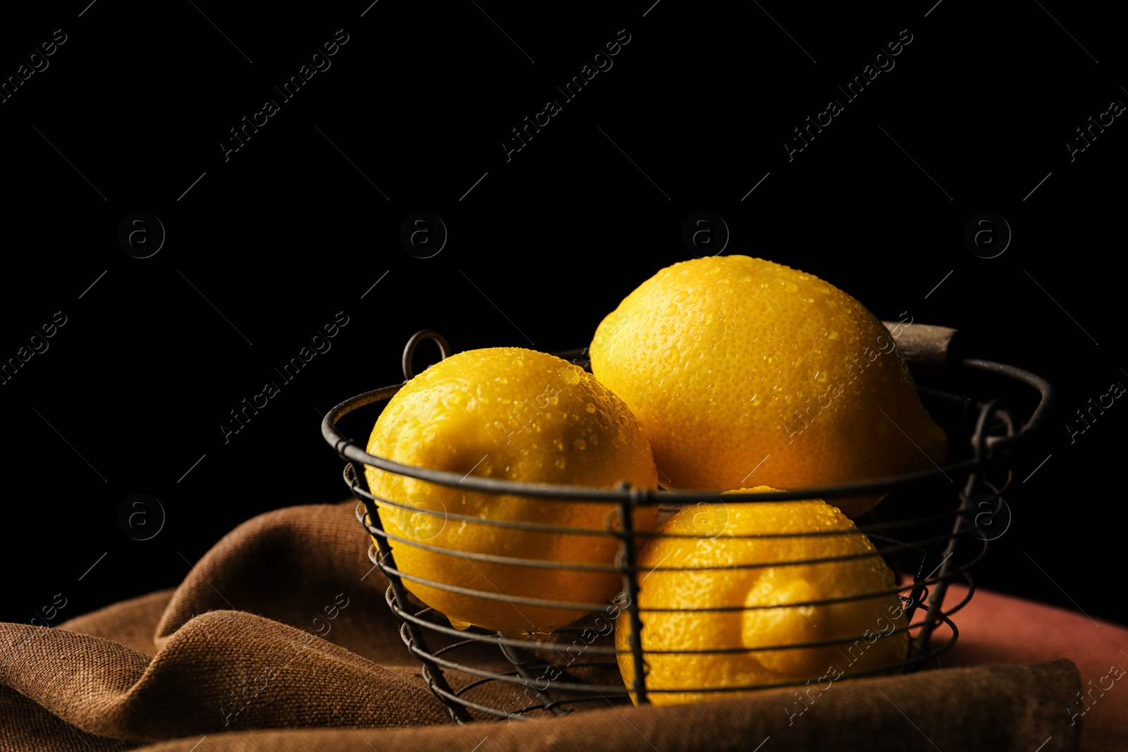 Photo of Basket with whole lemons on table against dark background