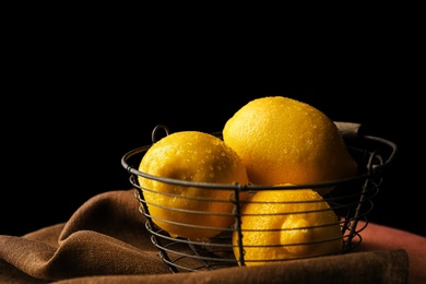 Photo of Basket with whole lemons on table against dark background