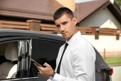 Attractive young man with smartphone near luxury car outdoors