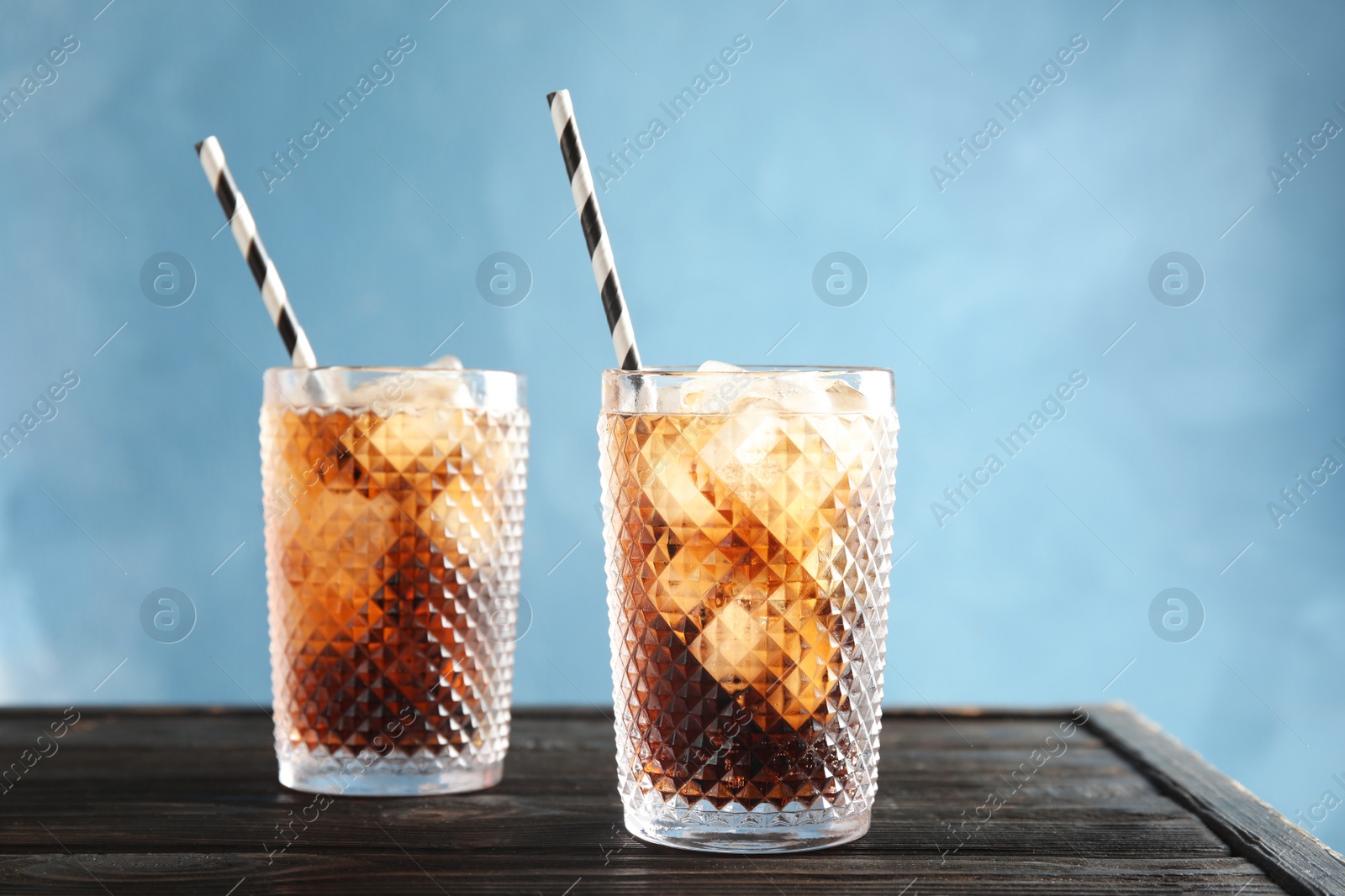 Photo of Glasses of refreshing cola with ice cubes and straws on table