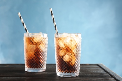 Glasses of refreshing cola with ice cubes and straws on table