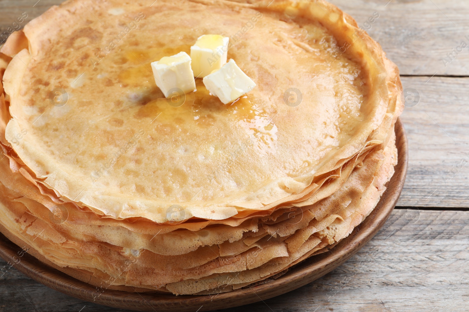 Photo of Stack of delicious crepes with melting butter on wooden table, closeup