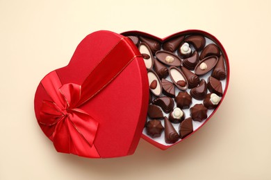Photo of Heart shaped box with delicious chocolate candies on beige background, top view