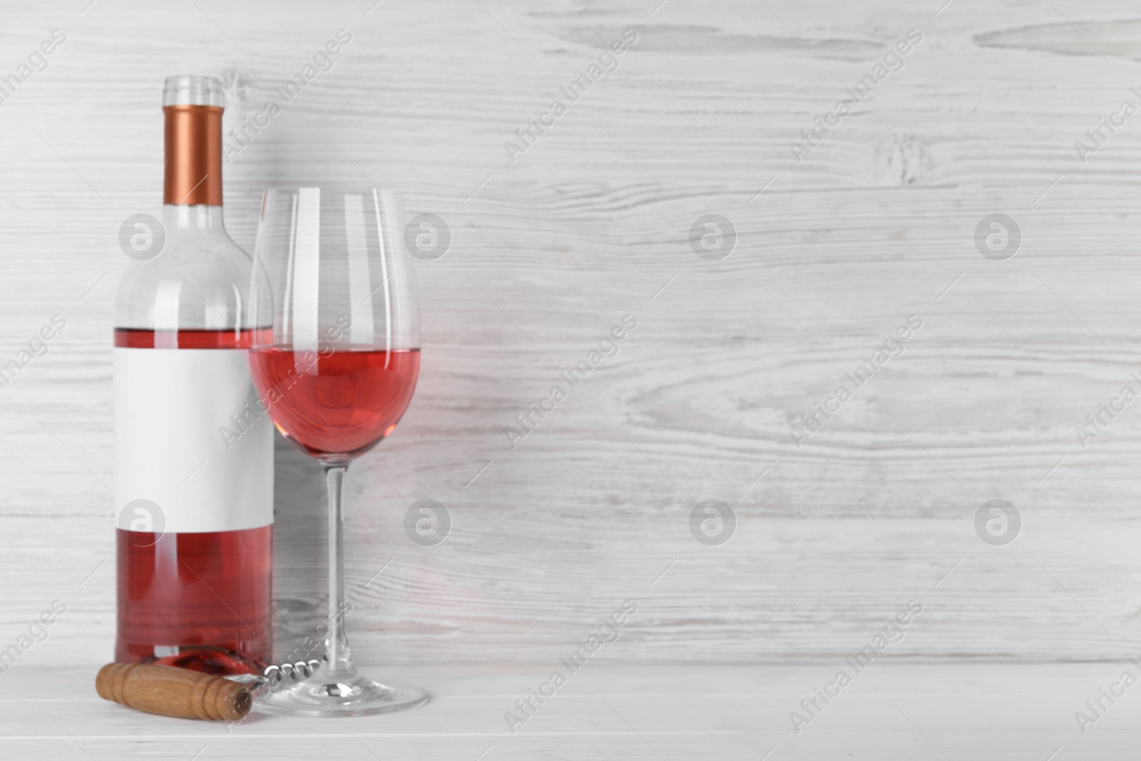 Photo of Corkscrew near bottle and glass of delicious rose wine on table against white wooden background. Space for text