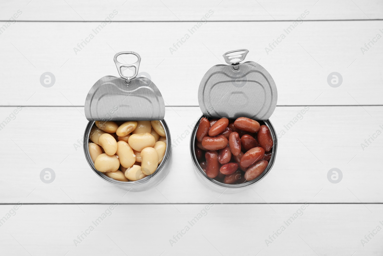 Photo of Tin cans with different canned kidney beans on white wooden table, flat lay