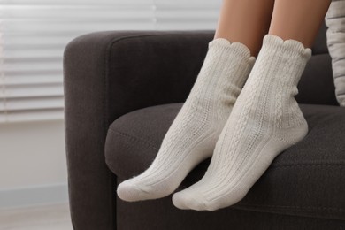 Woman in warm socks relaxing on armchair at home, closeup. Space for text