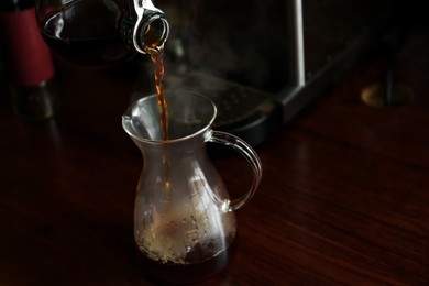 Photo of Pouring coffee into glass jug on wooden table in cafe