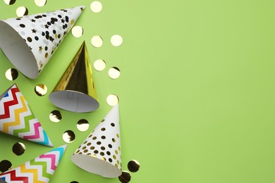 Photo of Bright party hats and shiny confetti on light green background, flat lay. Space for text