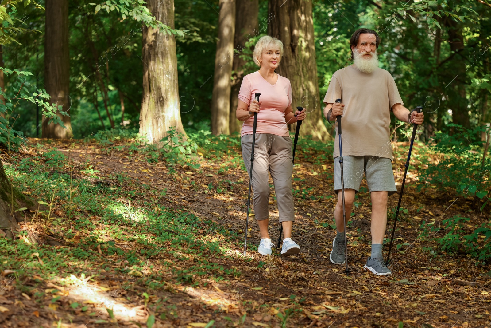 Photo of Senior man and woman performing Nordic walking in forest. Low angle view