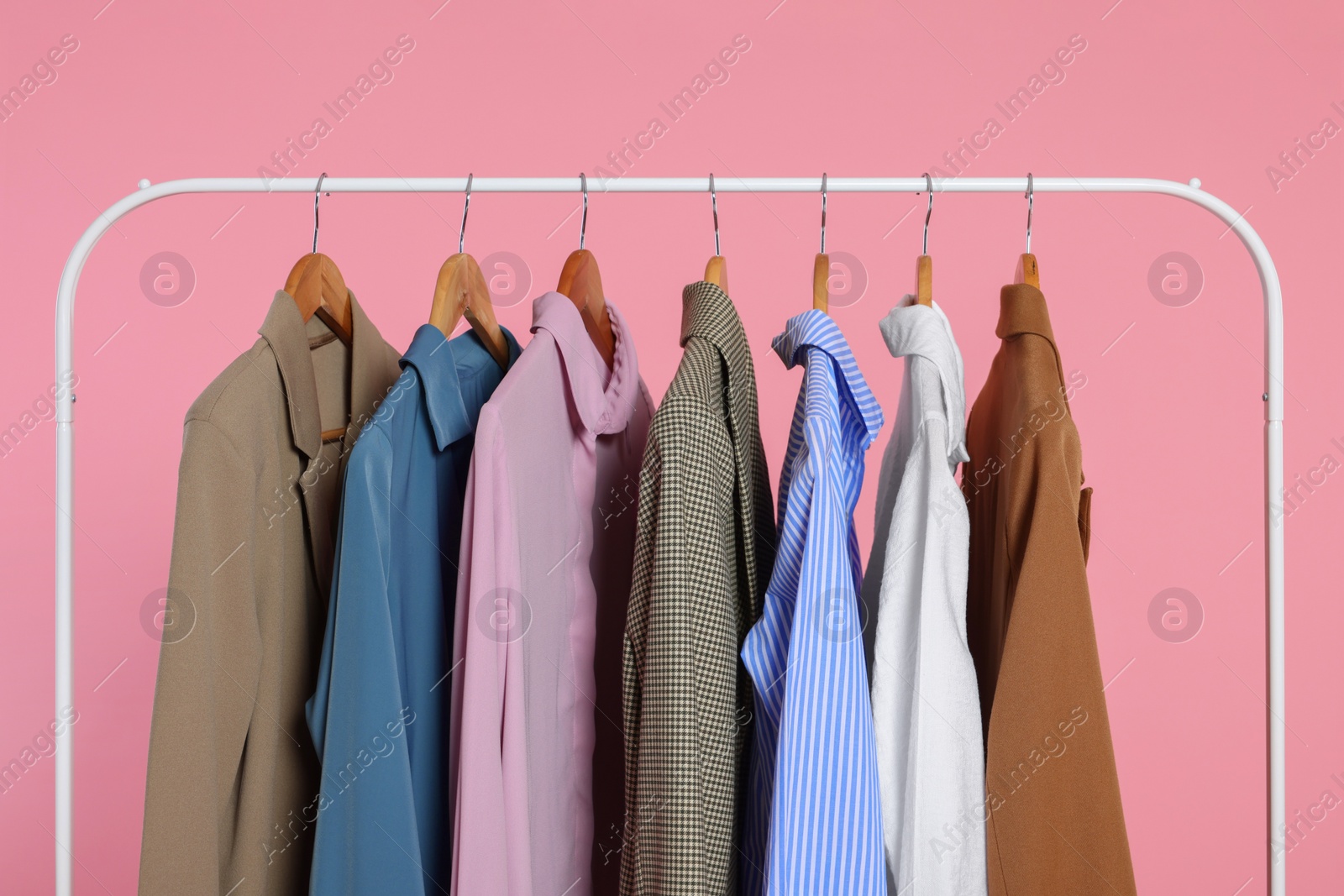 Photo of Rack with stylish clothes on wooden hangers against pink background