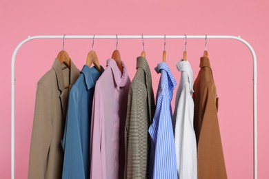 Photo of Rack with stylish clothes on wooden hangers against pink background