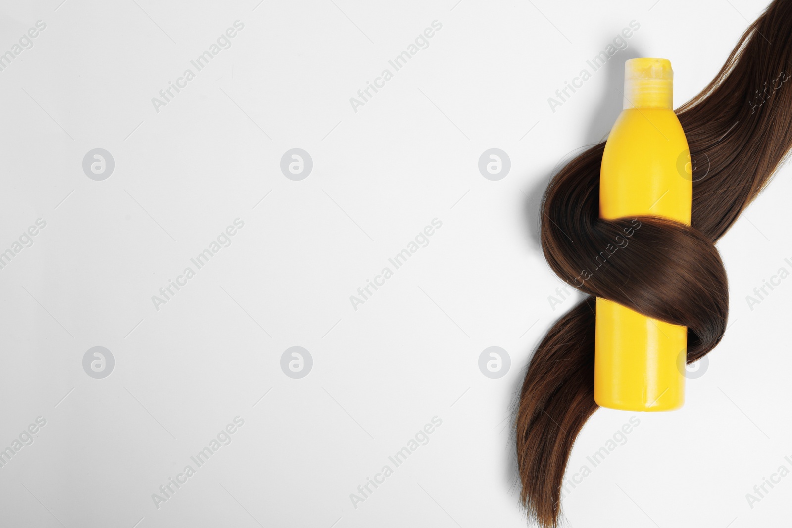 Photo of Shampoo bottle wrapped in lock of hair isolated on white, top view. Natural cosmetic products