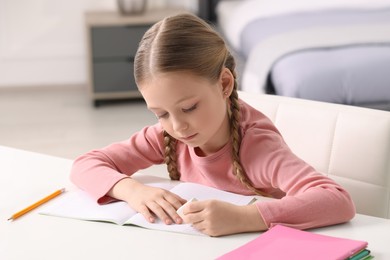 Girl using eraser at white desk in room