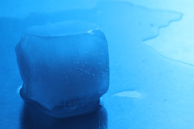 Crystal clear ice cube on light blue background, closeup with space for text. Color tone effect