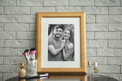 Black and white portrait of happy young couple in photo frame on table near white wall