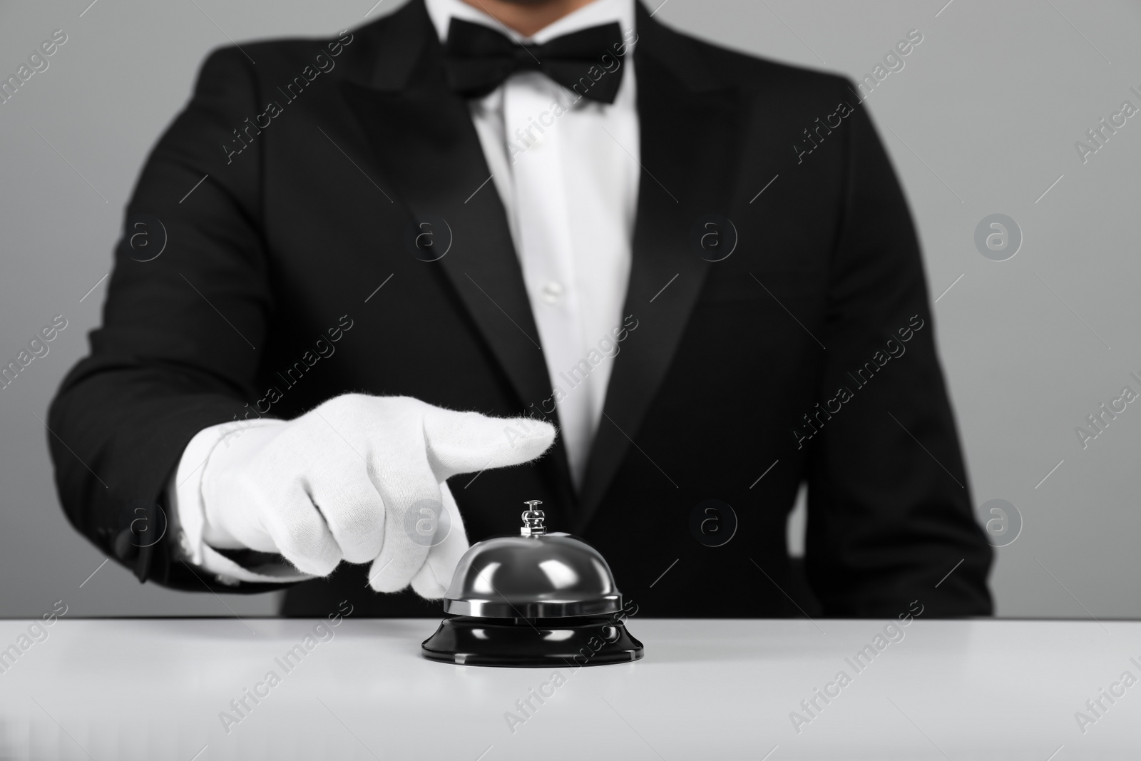 Photo of Butler ringing service bell at white table, closeup