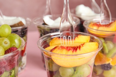 Photo of Fresh tasty fruit salad in plastic cups on pink background, closeup