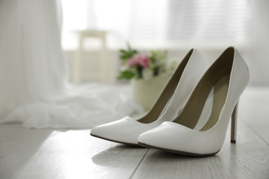 Photo of Pair of white high heel shoes and blurred wedding dress on background, space for text