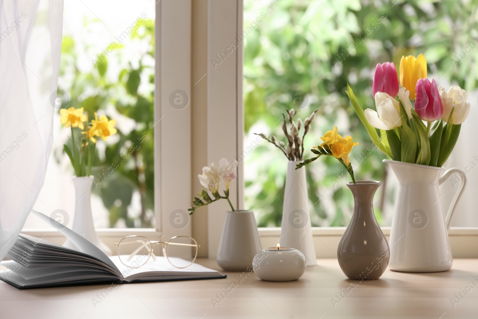 Photo of Different beautiful spring flowers, burning candle and book on window sill