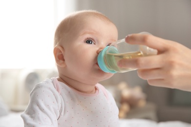 Photo of Lovely mother giving her baby drink from bottle in room