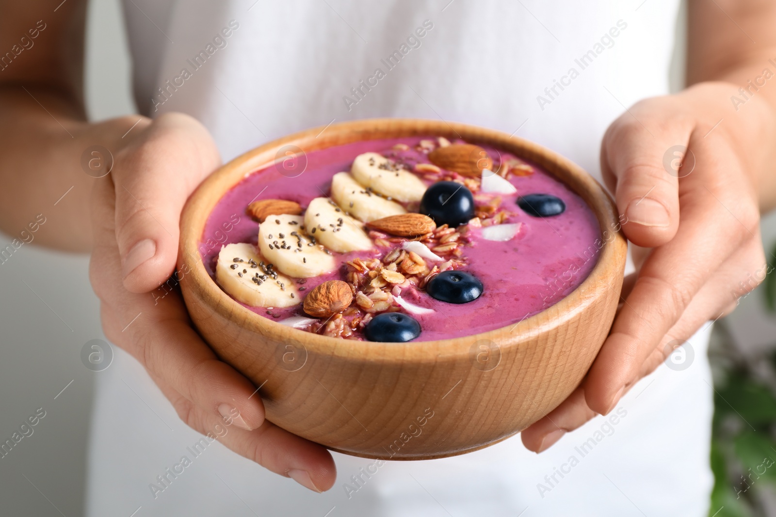 Photo of Woman holding dessert bowl with delicious acai smoothie, closeup view