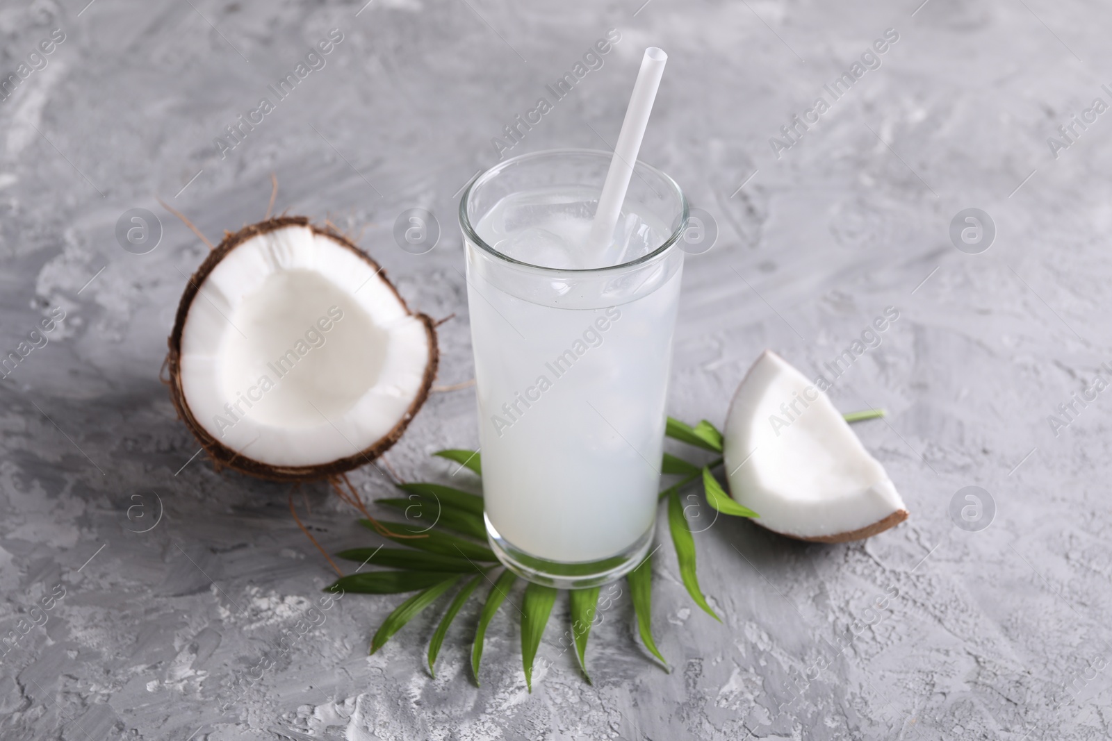 Photo of Glass of coconut water with ice cubes, palm leaf and nut on grey table