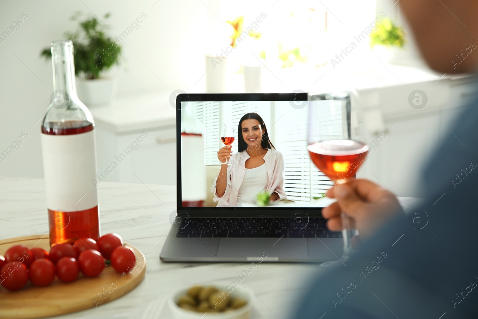 Photo of Friends drinking wine while communicating through online video conference in kitchen. Social distancing during coronavirus pandemic