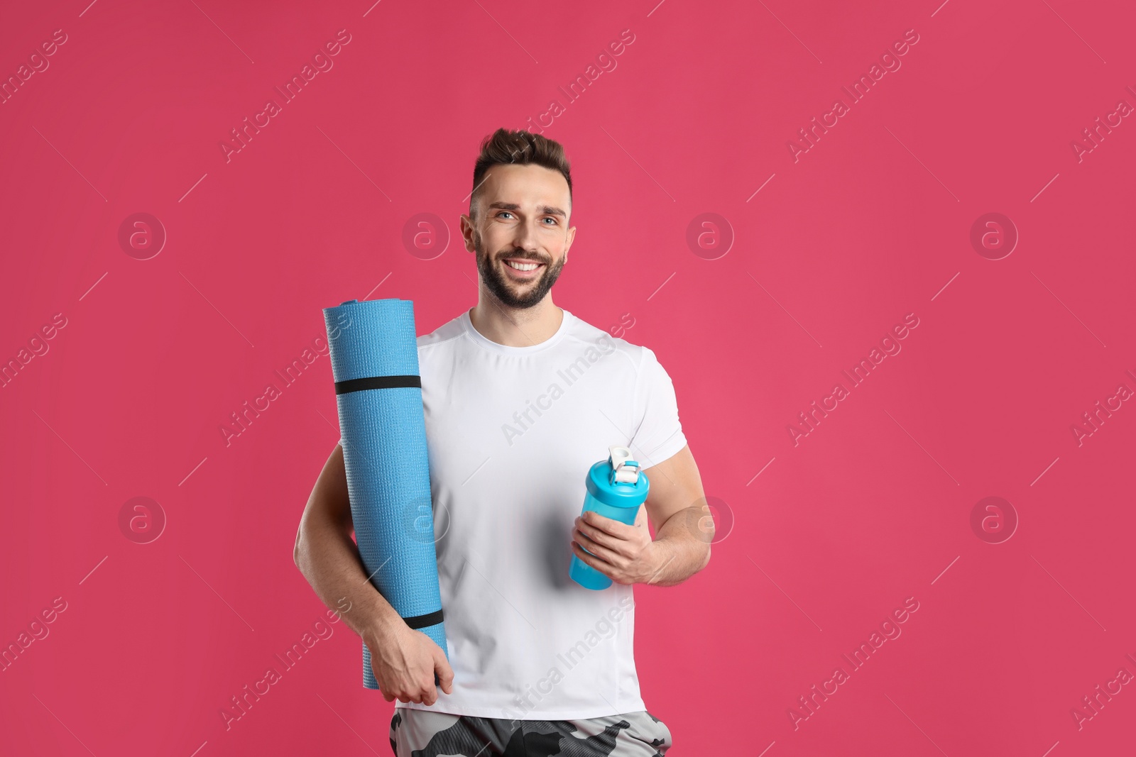 Photo of Handsome man with yoga mat and shaker on pink background