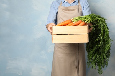 Photo of Woman holding wooden crate with fresh ripe carrots against color background. Space for text