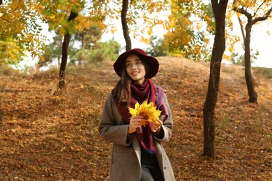 Young beautiful woman with hat and leaves in park. Autumn walk