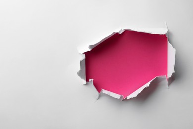 Hole in white paper on pink background, space for text