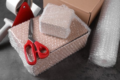 Photo of Cardboard boxes, bubble wrap, adhesive tape and scissors on dark grey table