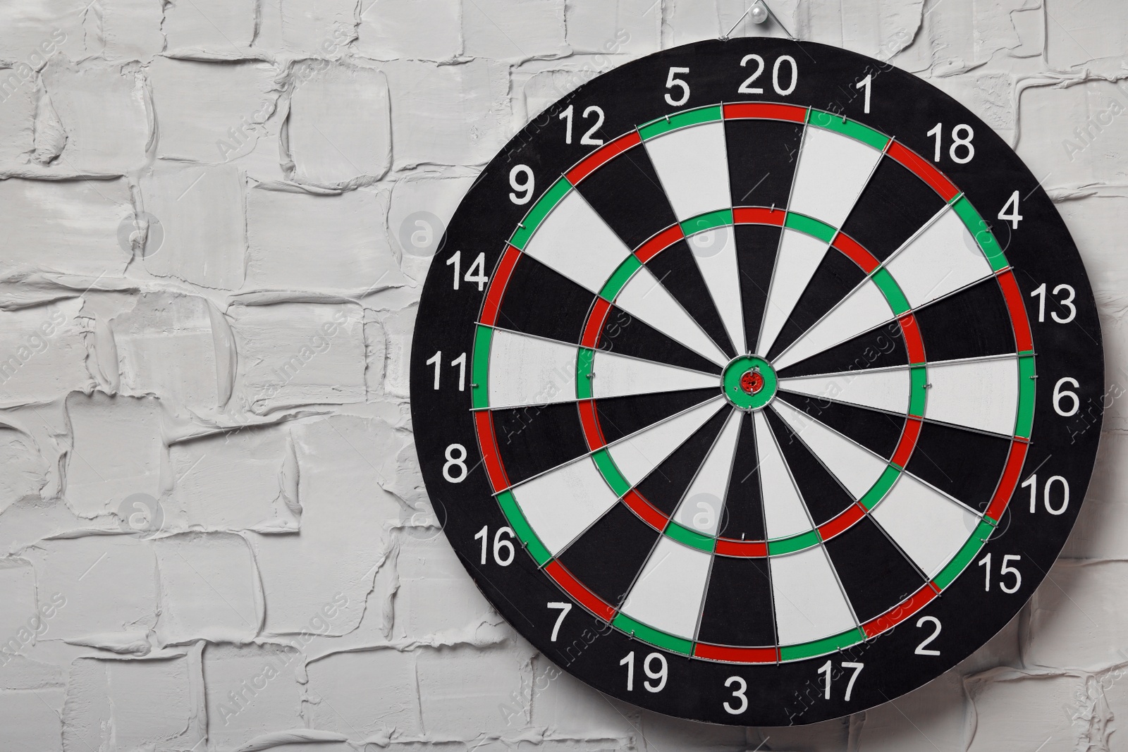 Photo of Dart board hanging on white textured wall. Space for text