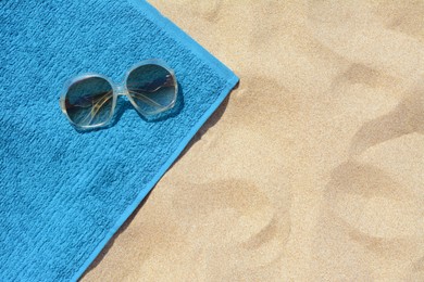 Soft blue beach towel with sunglasses on sand, top view. Space for text