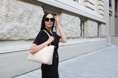 Young woman with stylish bag on city street, space for text