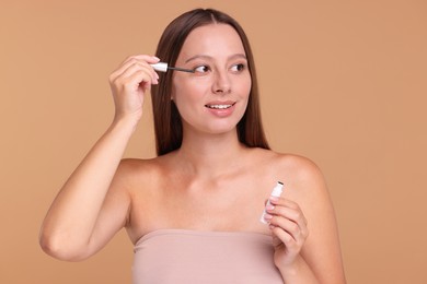 Beautiful woman applying serum onto eyelashes on beige background