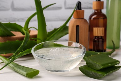 Photo of Bowl of cosmetic gel and cut aloe vera leaves on white wooden table, closeup