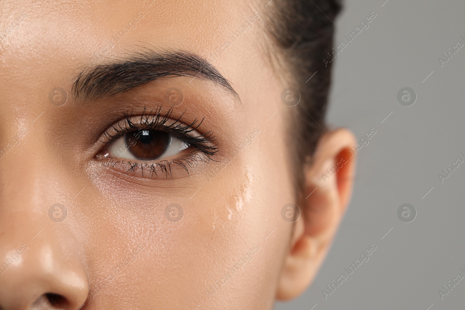 Photo of Woman with eye cream on grey background, closeup. Skin care