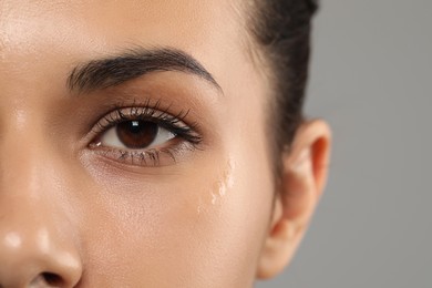 Woman with eye cream on grey background, closeup. Skin care