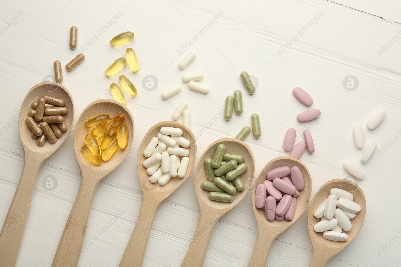 Photo of Different vitamin capsules in spoons on white wooden table, flat lay. Space for text