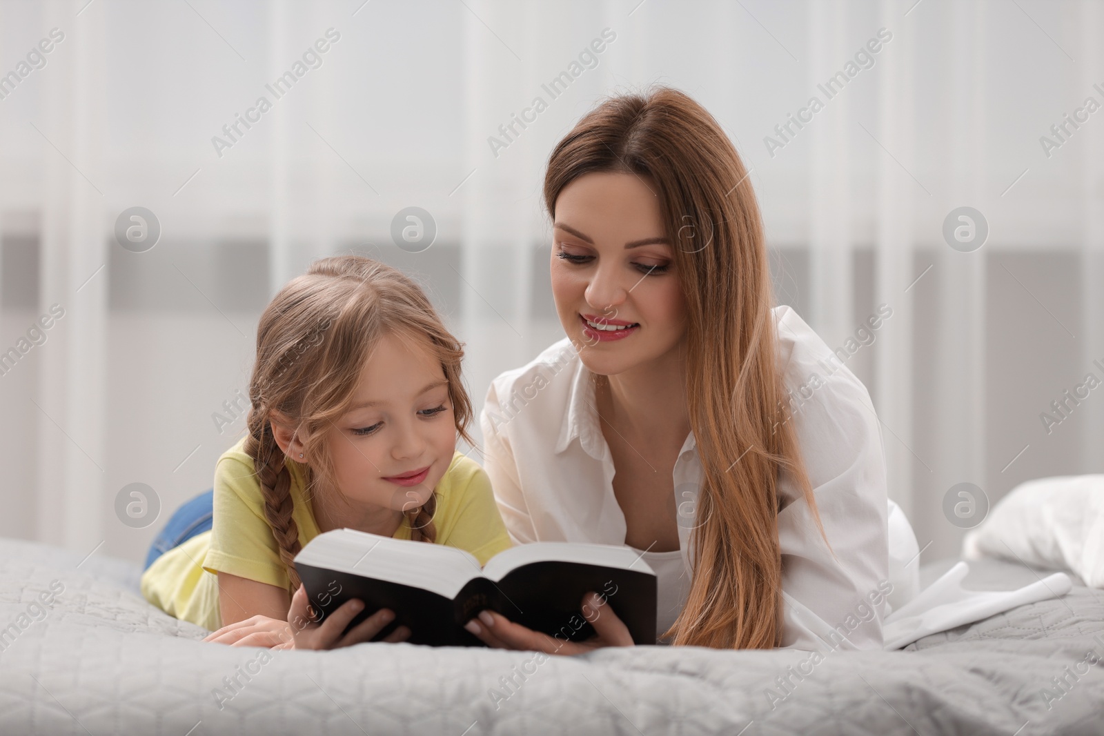 Photo of Girl and her godparent reading Bible together on bed at home