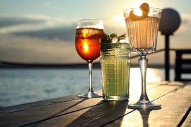 Glasses of fresh summer cocktails on wooden table outdoors at sunset, low angle view. Space for text