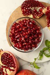 Photo of Ripe juicy pomegranate grains and green leaves on white marble table, flat lay