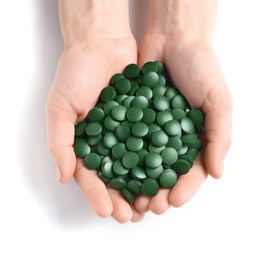 Woman holding heap of green spirulina pills on white background, top view