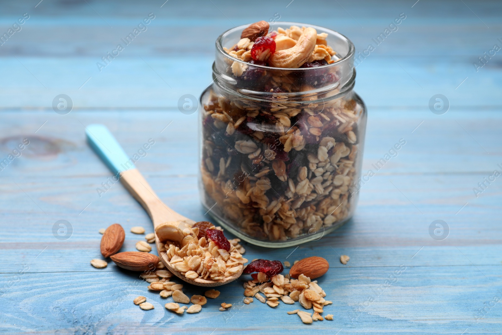 Photo of Jar of tasty granola with nuts and dry fruits on light blue wooden table