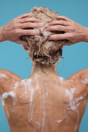 Woman washing hair on light blue background, back view