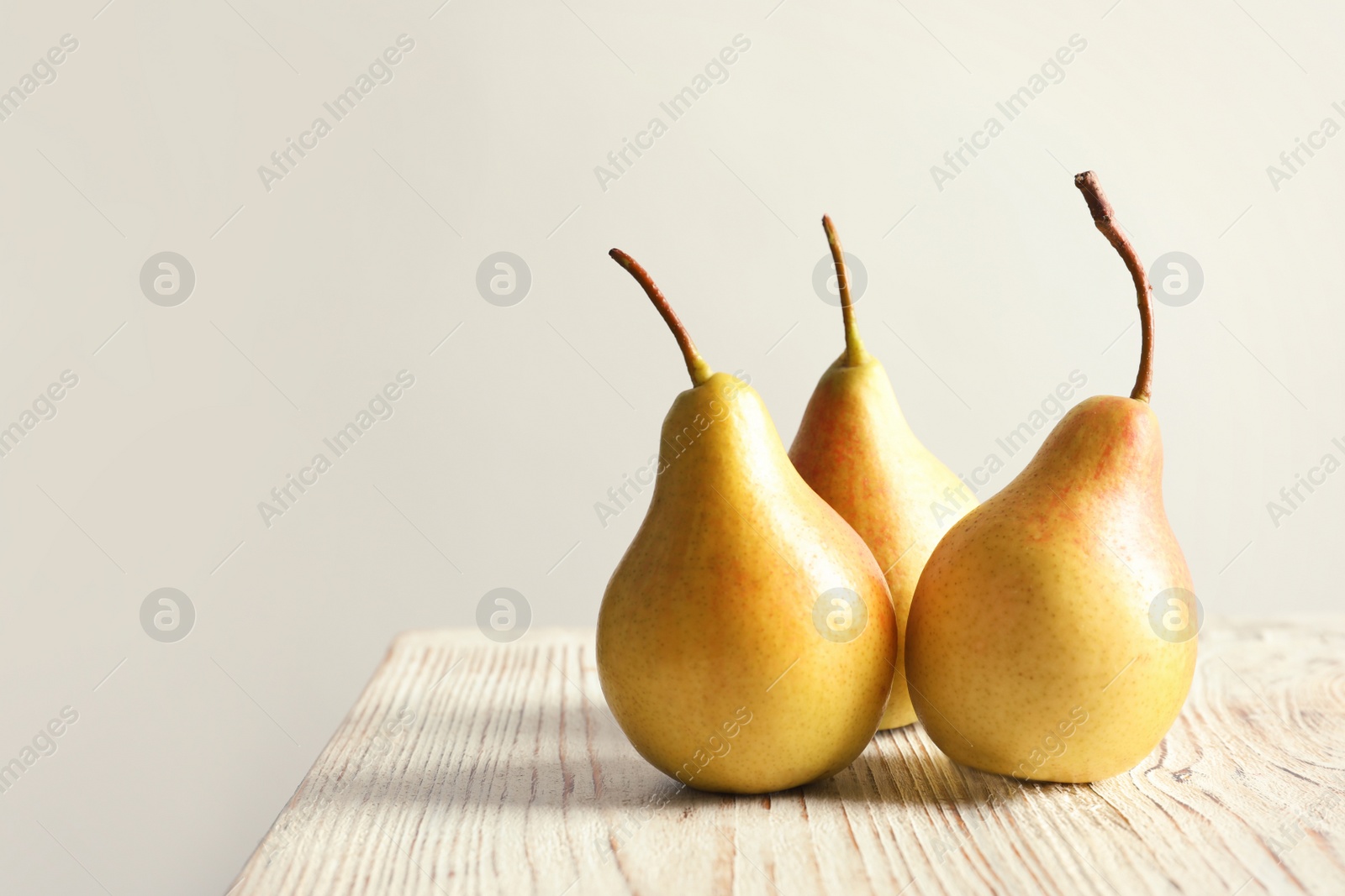 Photo of Ripe pears on wooden table against light background. Space for text