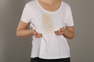 Photo of Woman showing stain from coffee on her shirt against light grey background, closeup