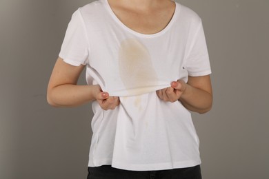 Woman showing stain from coffee on her shirt against light grey background, closeup