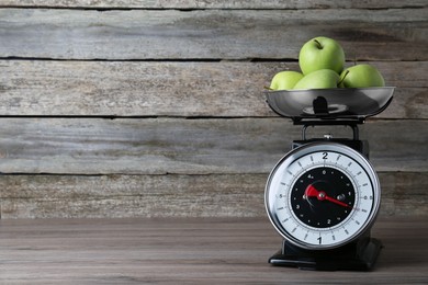 Kitchen scale with green apples on wooden table. Space for text